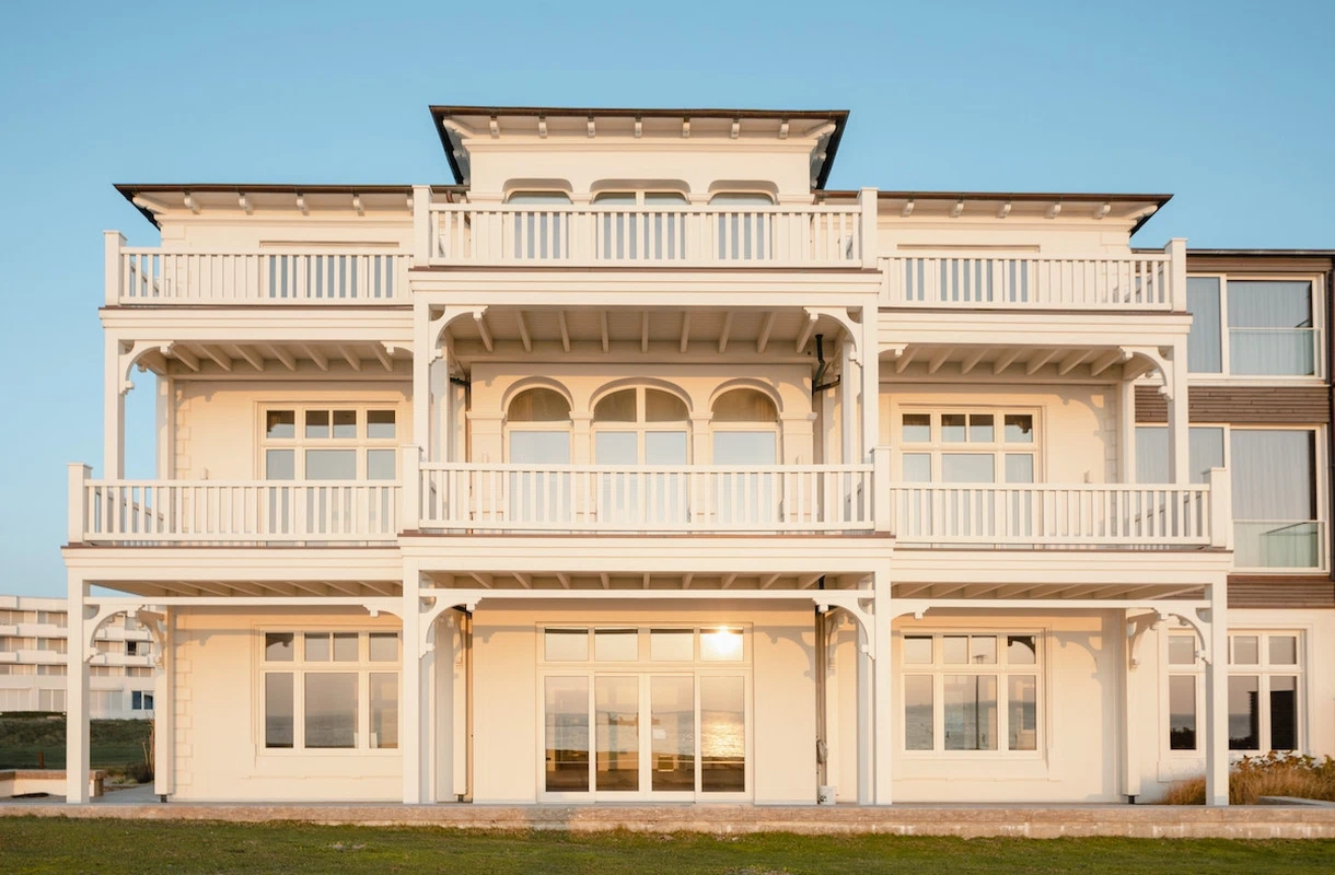 Außenansicht eines weißen, dreistöckigen Gebäudes in Bäderarchitektur mit Balkonen bei untergehender Sonne