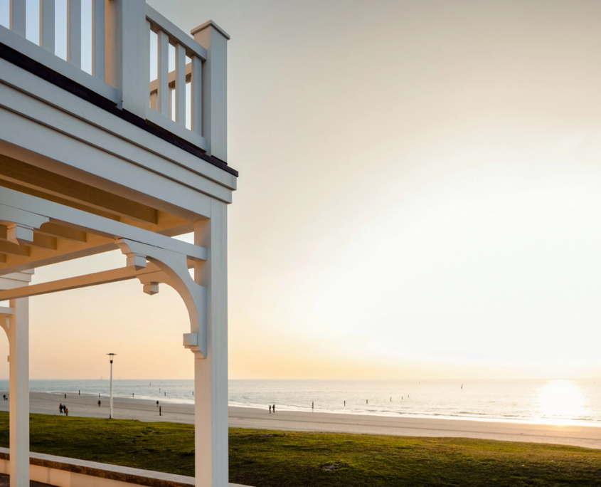 Holzveranda des 1884 Norderney mit Blick auf die Nordsee und den Sandstrand bei Sonnenuntergang