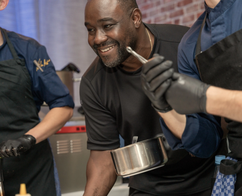 Nelson Müller lächelt beim Kochen mit seinen Kollegen